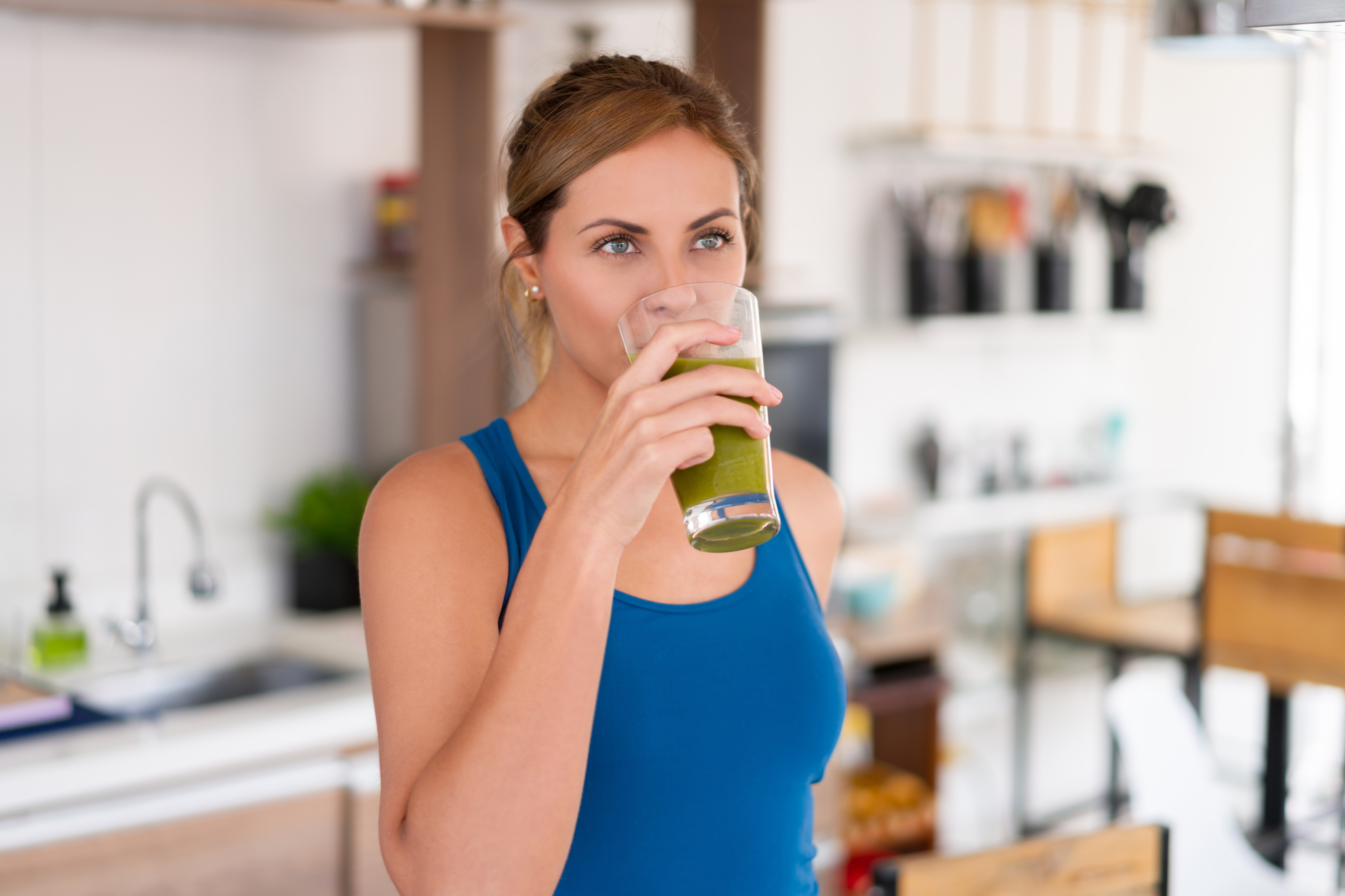 A woman drinking a glass of MTH (Moringa Total Health) green drink made from The MLM Shoppe supplement formula.